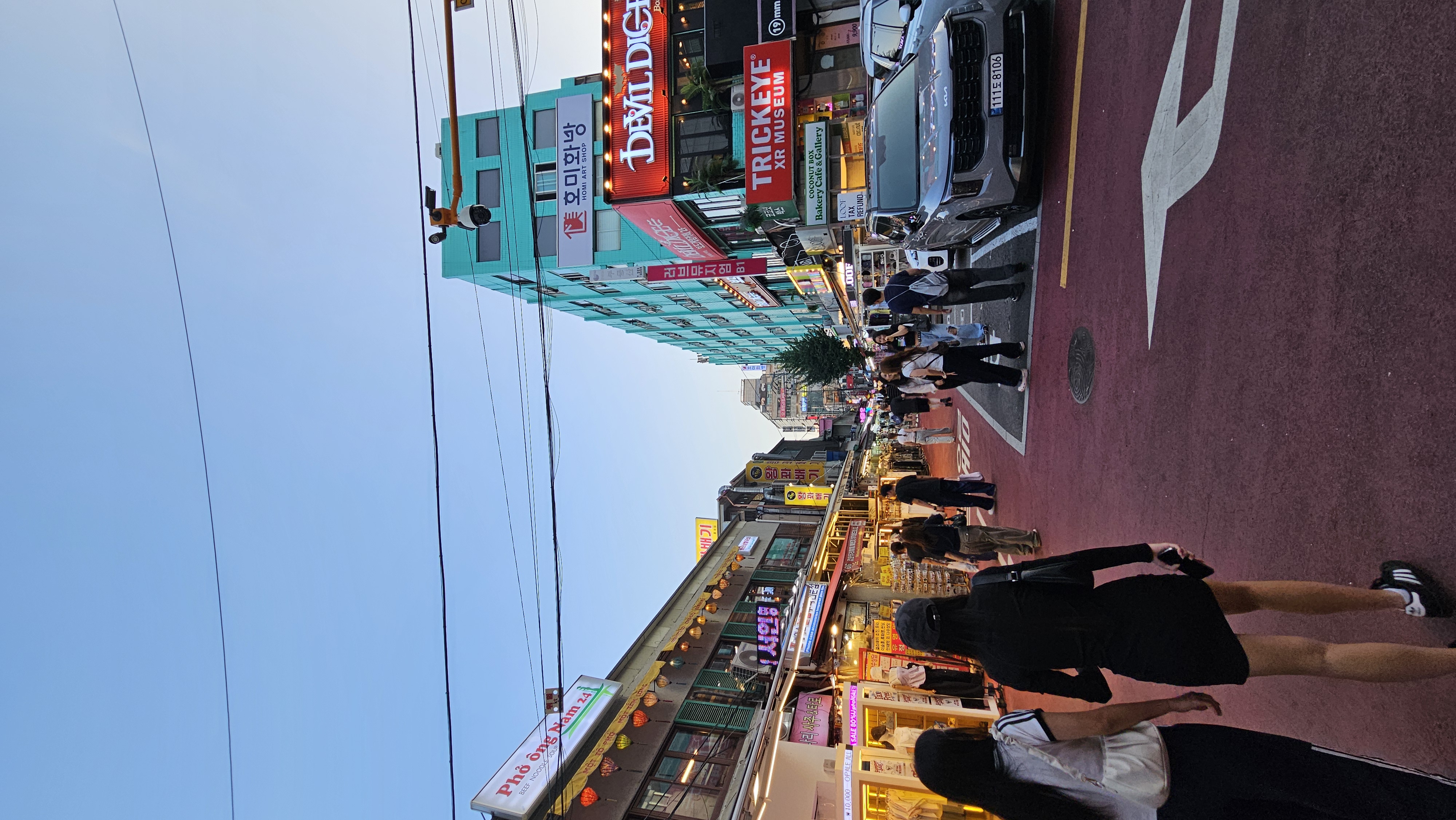 Pedestrians and illuminated shopfronts on a Hongdae street at dusk